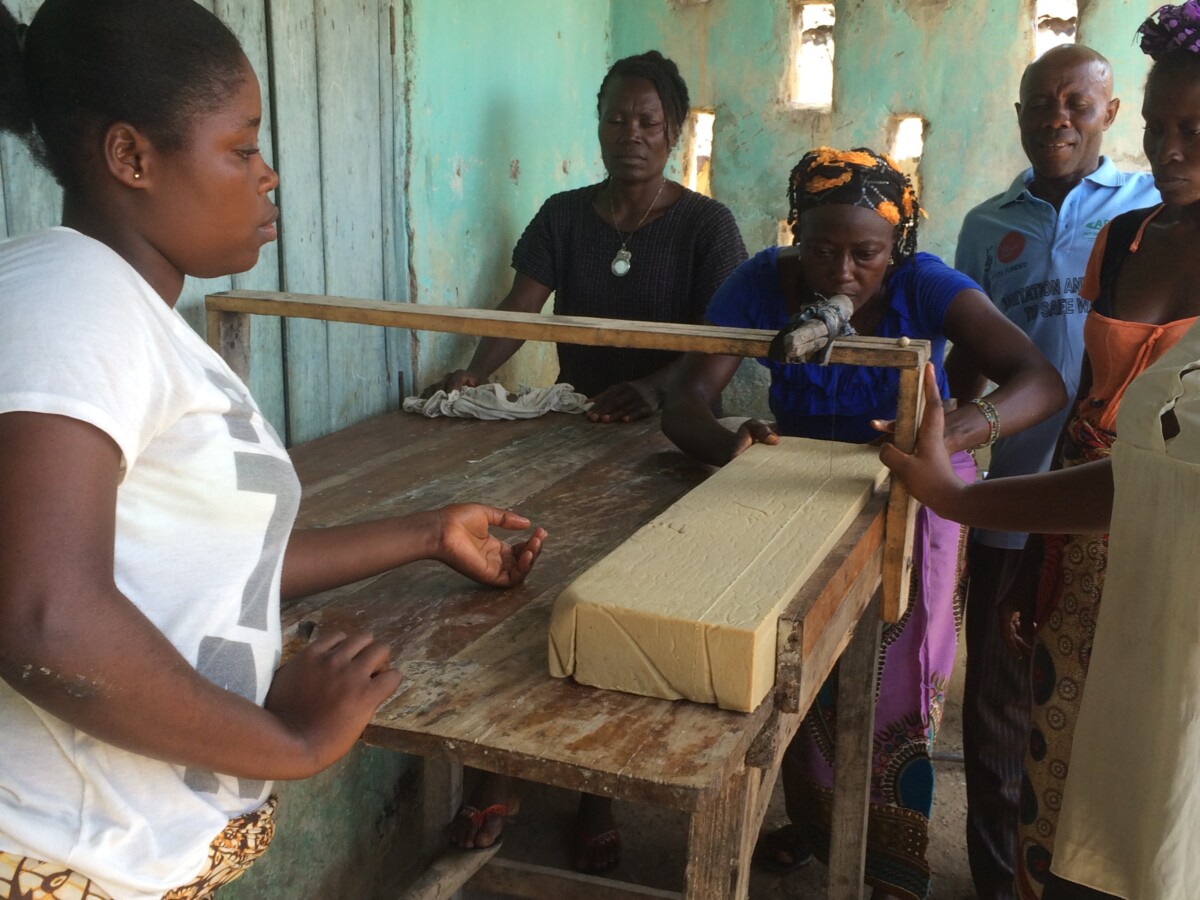 Four women stand around a work table on which is placed a large block of soap, which they are processing.