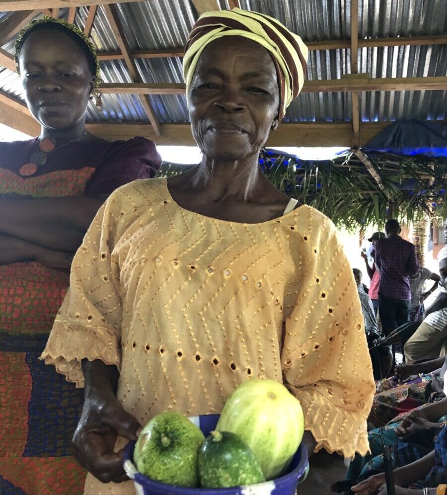 A lady in orange holds a bowl of green fruit to the camera.