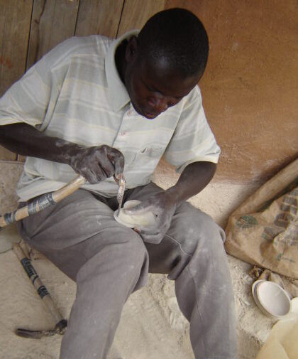 A seated man works clay into a bowl shape.