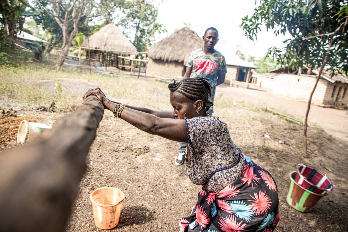 A woman pushes a big wooden lever to crush palm seeds.